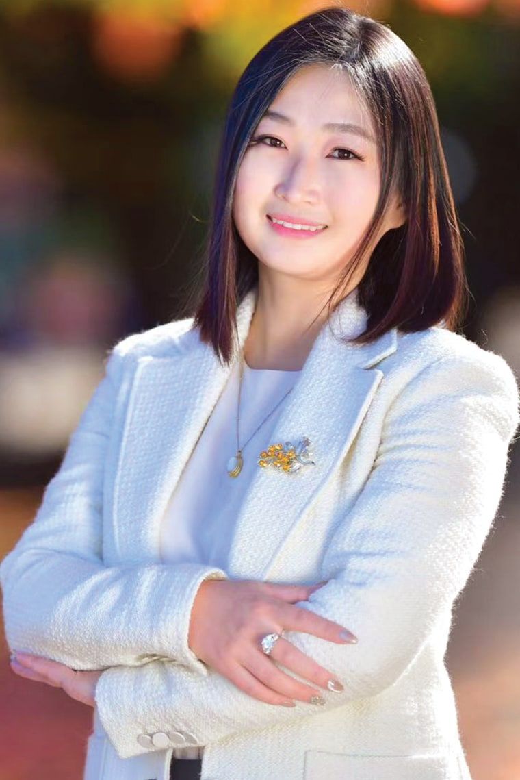 Avery Quan,身穿白色西装外套,面带微笑,背景是秋天的树